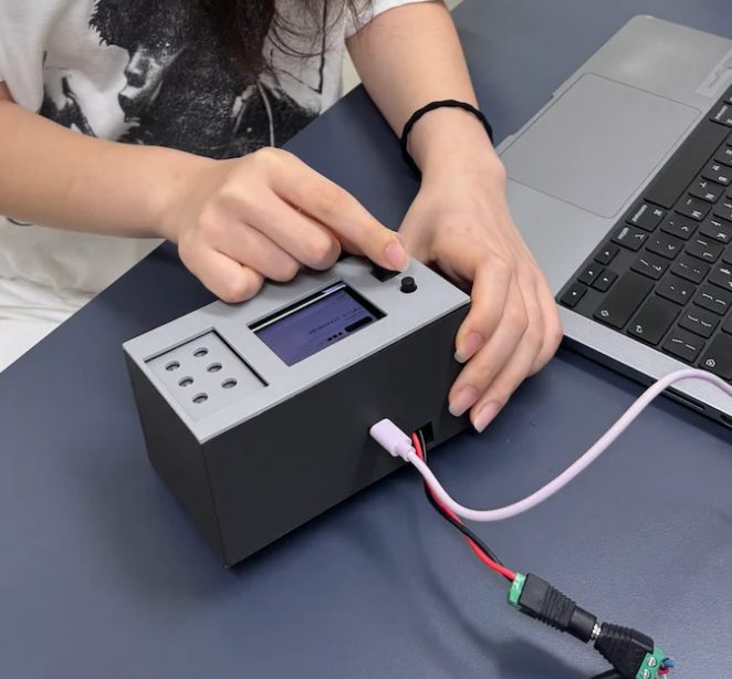 Hands pressing a button on a black screen-description device connected to a laptop.