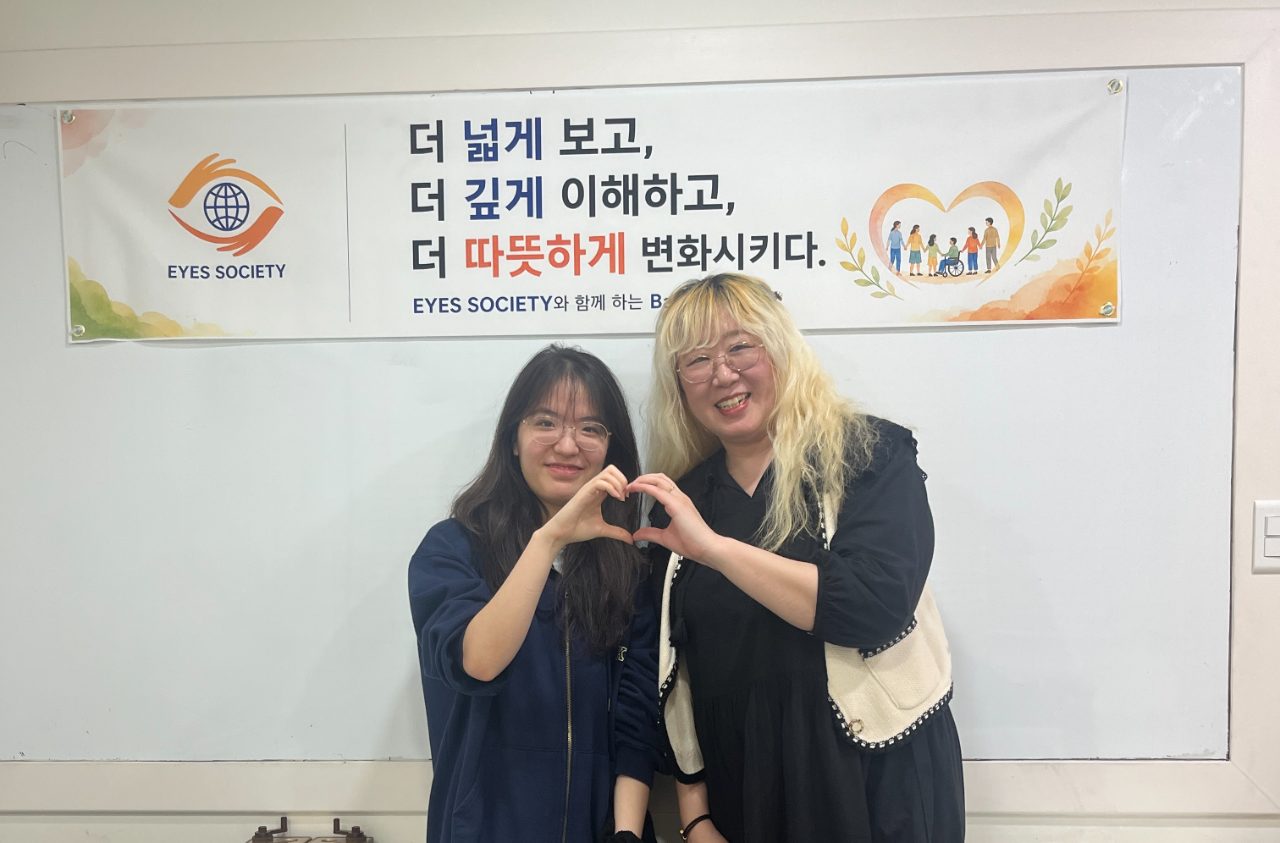 Two people making a heart with their hands in front of the EYES Society banner.
